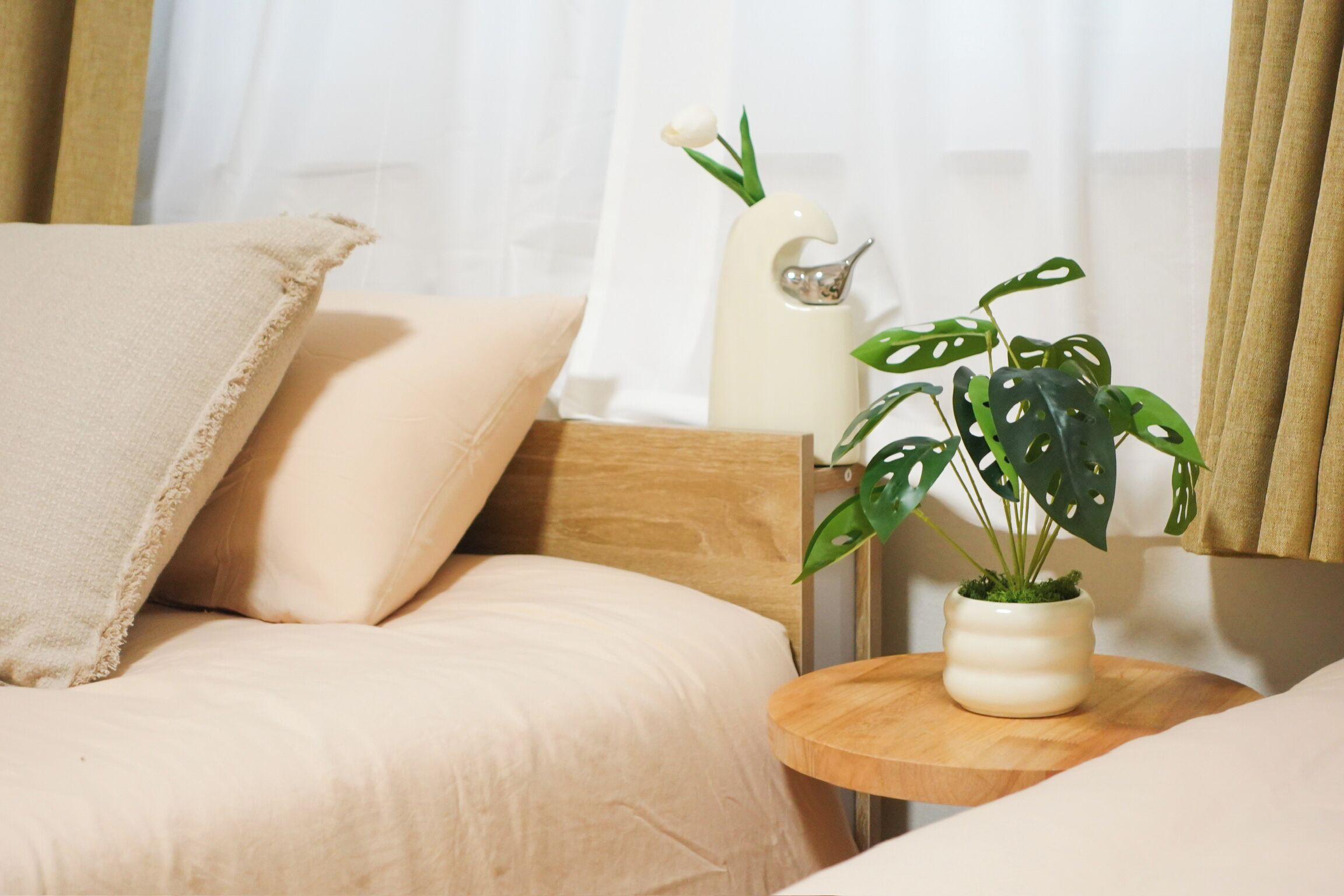 Une chambre à coucher avec un lit, des oreillers, une table de chevet ornée d’une plante et un vase.