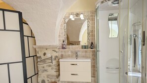 Un baño con cabina de ducha de vidrio, un lavabo con espejo y un pequeño cubo de basura.
