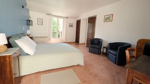 Un dormitorio con una cama, dos sillas, una mesita, una mesilla de noche, una ventana con cortinas y una puerta.