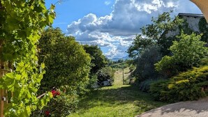Un sendero de jardín bajo un arco de piedra con follaje y cielo despejado.