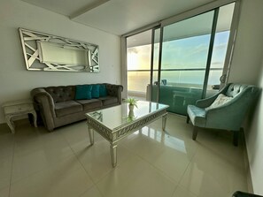 Ein Wohnzimmer mit einer Couch, einem Couchtisch und einem Sessel, mit einem großen Fenster mit Meerblick.