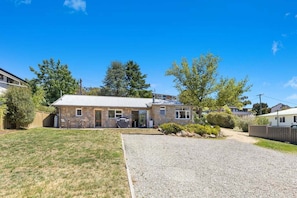 A two-story stone house with a gravel driveway, a small patio, and a fenced yard.