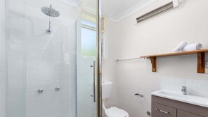 Et badeværelse med bruseniche, toilet, vask og en træhylde med håndklæder.