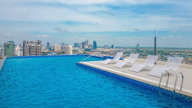 A swimming pool with lounge chairs and a city skyline in the background. - MERIDIAN Inn RESIDENCE  (Phnom Penh)