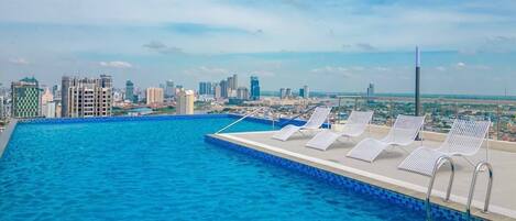 A swimming pool with lounge chairs and a city skyline in the background.