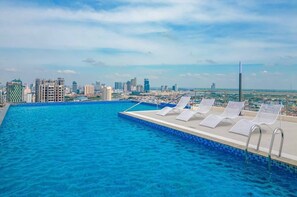 Ein Schwimmbecken mit Liegestühlen und einer Stadtkulisse im Hintergrund.