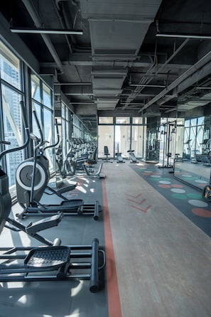 Ett gym med träningsutrustning, stora fönster och ett betonggolv.
