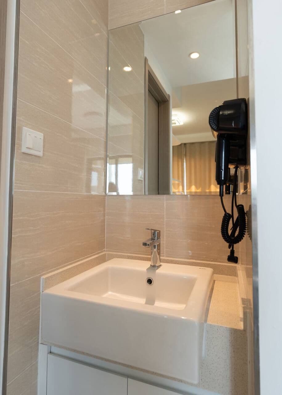Un baño con un lavamanos blanco, un espejo y un secador de pelo montado en la pared.