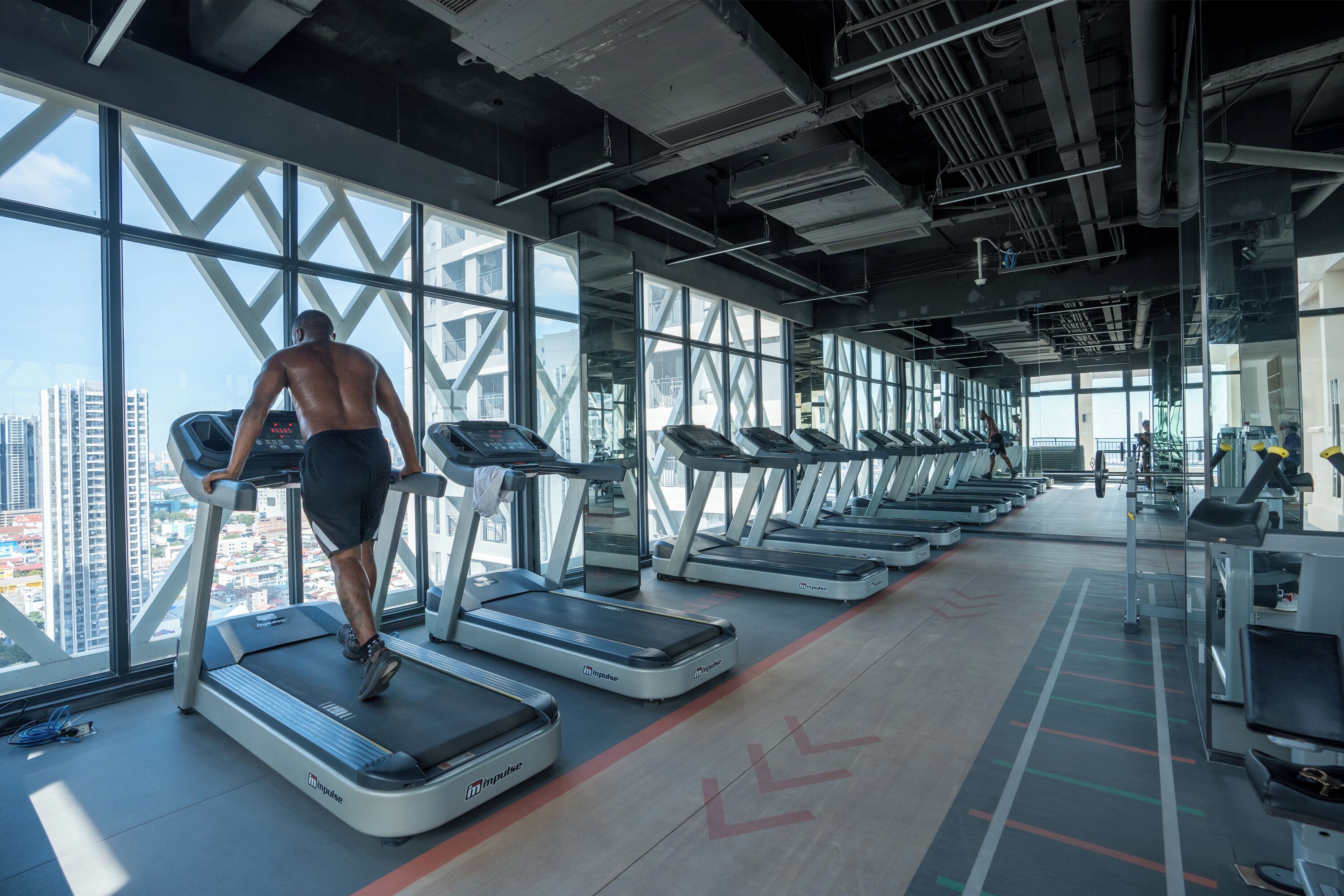 A gym with treadmills, a city view, and a high ceiling.