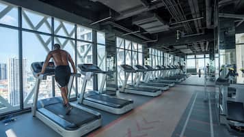 A gym with treadmills, a city view, and a high ceiling.