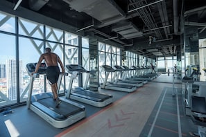 A gym with treadmills, a city view, and a high ceiling.