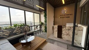 A reception area with a marble counter, a sofa with cushions, and a view of the city through large windows. - MERIDIAN Inn RESIDENCE  (Phnom Penh)