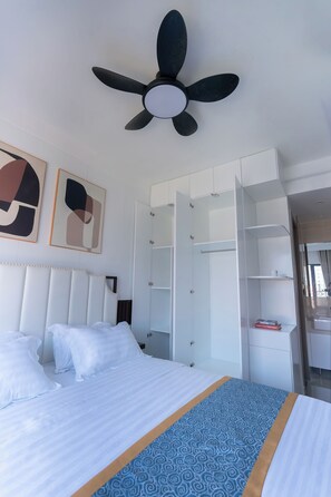 Ett hotellrum med en säng, en takfläkt, en garderob och abstrakt konst på väggen.