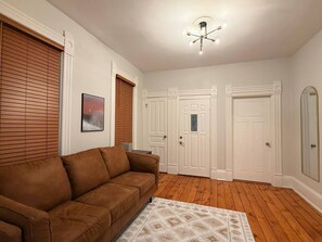 A living room with a brown sofa, a patterned rug, wooden flooring, white doors, and a ceiling light fixture. - EKO Stays | Holton Downtown Home Away from Home. (Milwaukee)