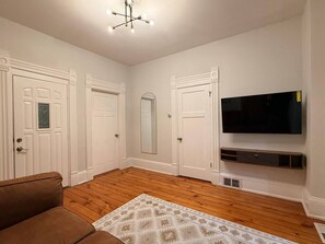 A living room with a brown sofa, a patterned rug, white doors, a large mirror, and a mounted TV. - EKO Stays | Holton Downtown Home Away from Home. (Milwaukee)