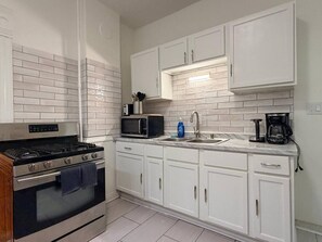A modern kitchen with white cabinetry, a stainless steel stove, a microwave, and a coffee maker. - EKO Stays | Holton Downtown Home Away from Home. (Milwaukee)