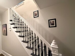 Un escalier avec des balustrades blanches et des rampes noires, menant à un palier où est fixée une applique murale blanche.