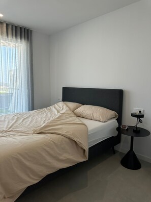 A modern hotel room with a bed, a bedside table with a clock, and a window with curtains. - Casa Seabre (Finestrat)
