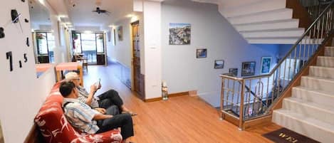 A hotel lobby with a reception desk, a staircase, and a waiting area with a red sofa.
