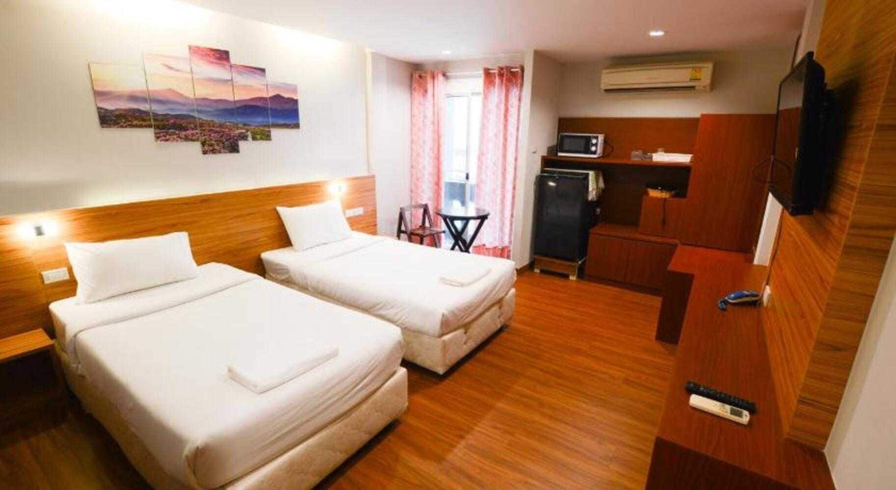 A hotel room with two beds, a desk, a chair, a TV, and an air conditioning unit.
