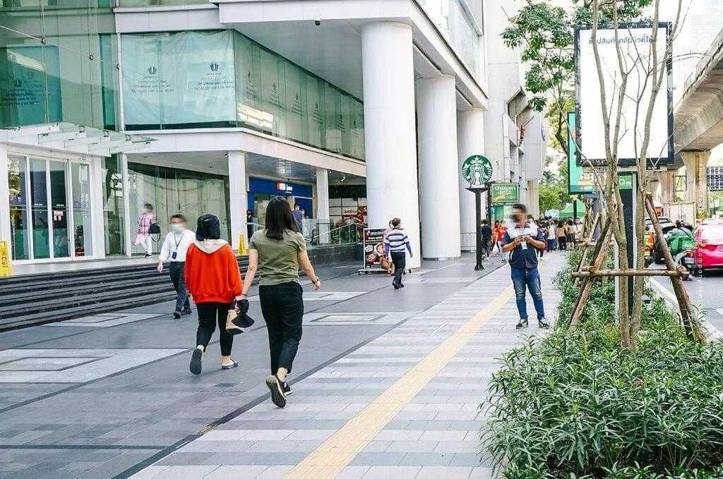 A pedestrian walkway with a Starbucks sign, a modern building with large windows, and a tree planter structure.