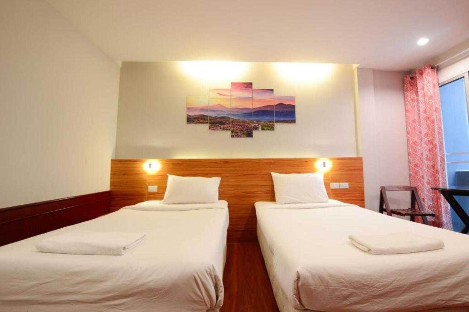 A hotel room with two beds, a wooden headboard, a painting above the beds, and a window with curtains.