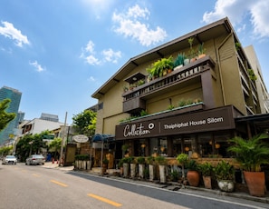 Ein Gebäude mit einem Schild, auf dem 'Collectian Thaiiphat House Silom' steht, und Balkonen mit Blumentöpfen.