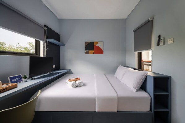 Ein modernes Zimmer mit einem Bett, einem Schreibtisch, einem Sessel, einem Fenster und einem an der Wand hängenden Kunstwerk.