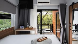 Une chambre d’hôtel comprenant un lit, une table de chevet avec un plateau, une télévision, un appareil de climatisation et un balcon donnant sur un espace verdoyant.