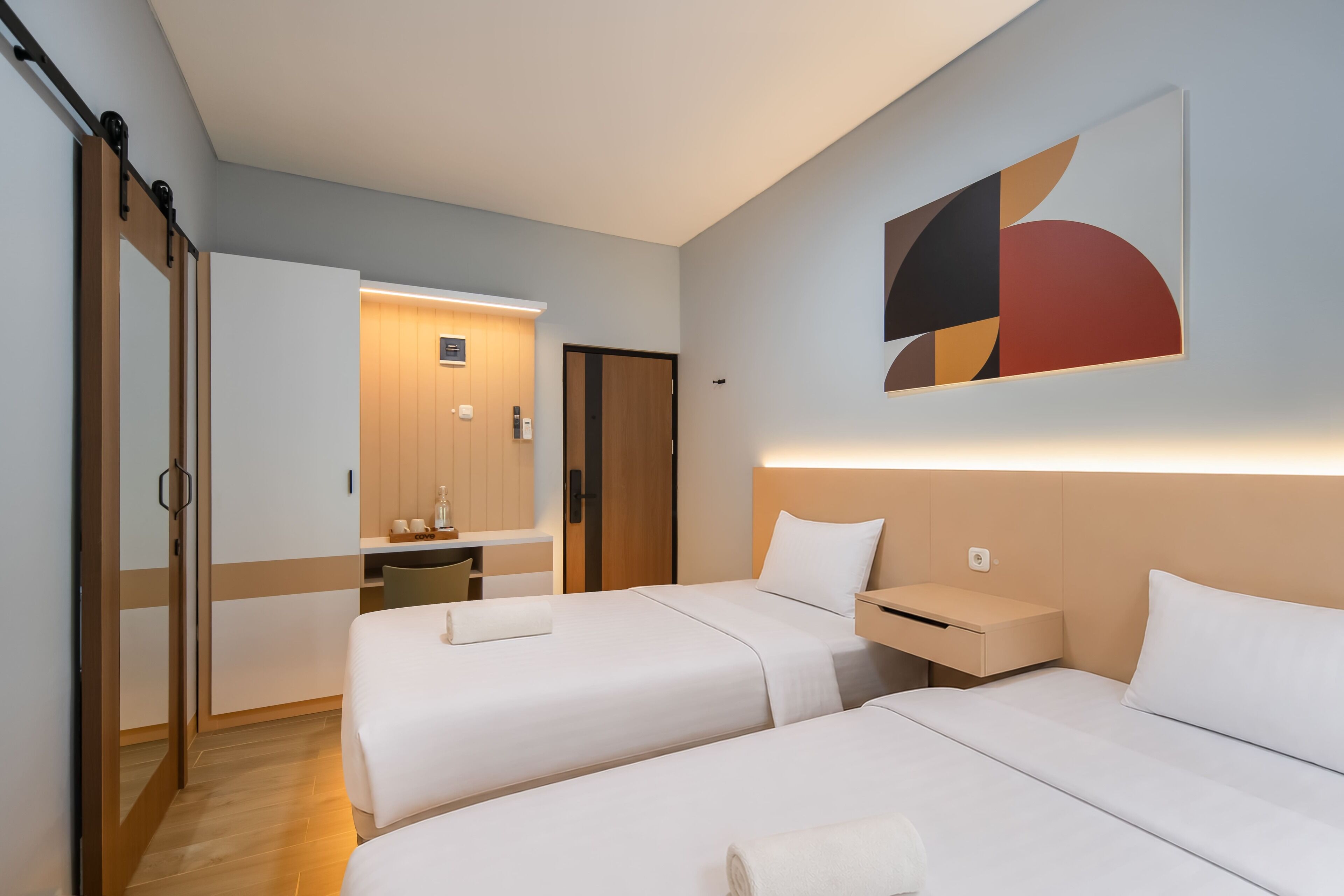 Habitación de hotel con dos camas, un escritorio, un espejo y una obra de arte abstracto colgada en la pared.