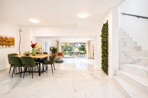 Un comedor moderno con piso de mármol, sillas verdes y una mesa con un florero.