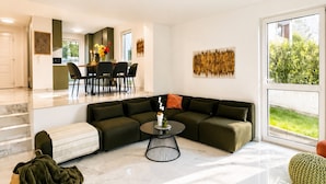A modern living room with a sectional sofa, a coffee table, and a dining area with chairs. - Elegant 4BR Villa w/ Garden & Terrace (Mödling)