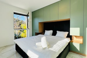 Une chambre moderne avec un grand lit, une fenêtre donnant sur la verdure et des murs verts.
