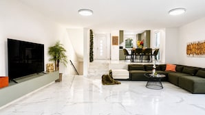 A modern living room with a flat-screen TV, a green sofa, a coffee table, and a staircase leading to a dining area. - Elegant 4BR Villa w/ Garden & Terrace (Mödling)