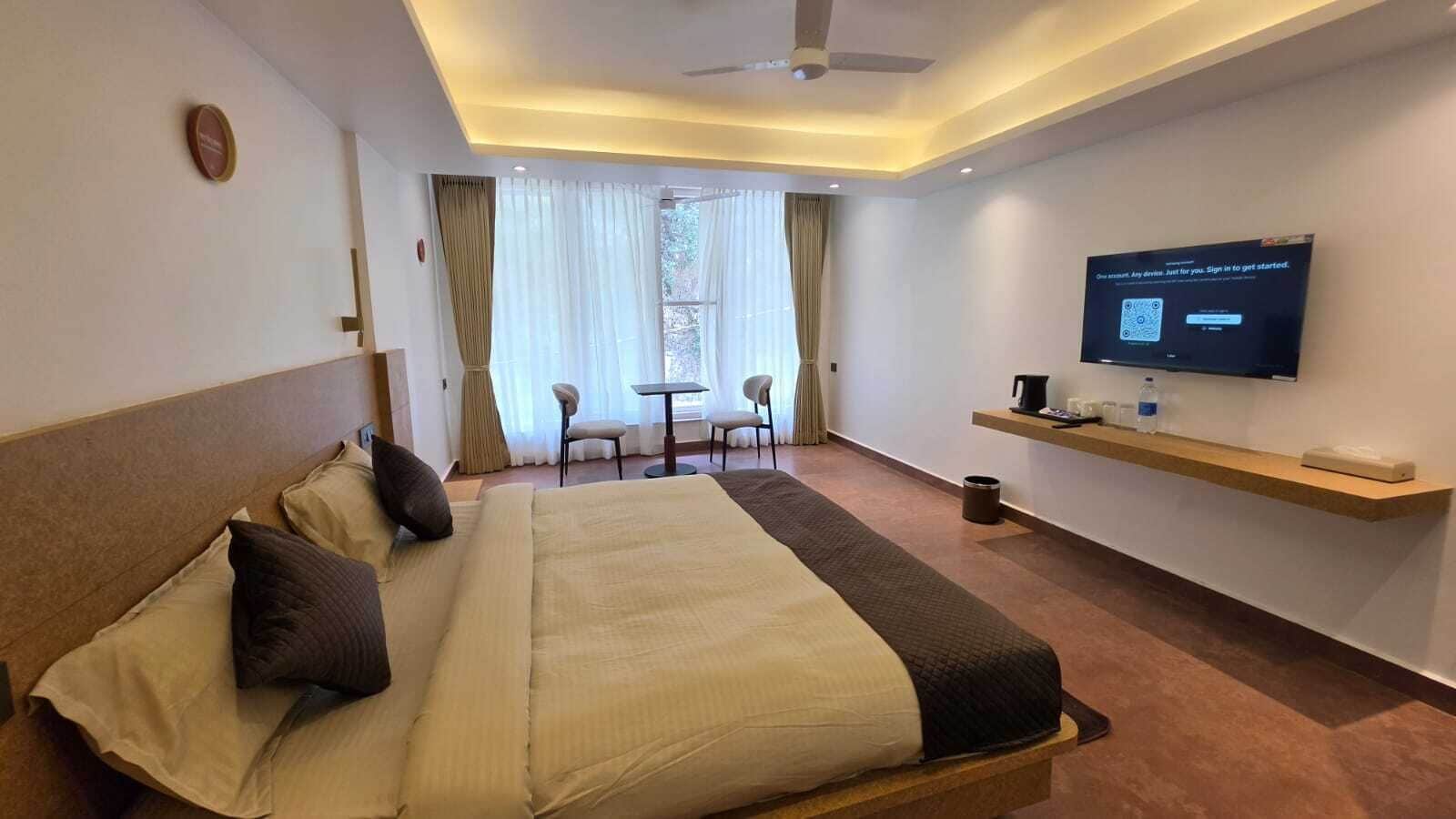 Hotellihuone, jossa on sänky, televisio, työpöytä ja ikkuna, jossa on verhot.