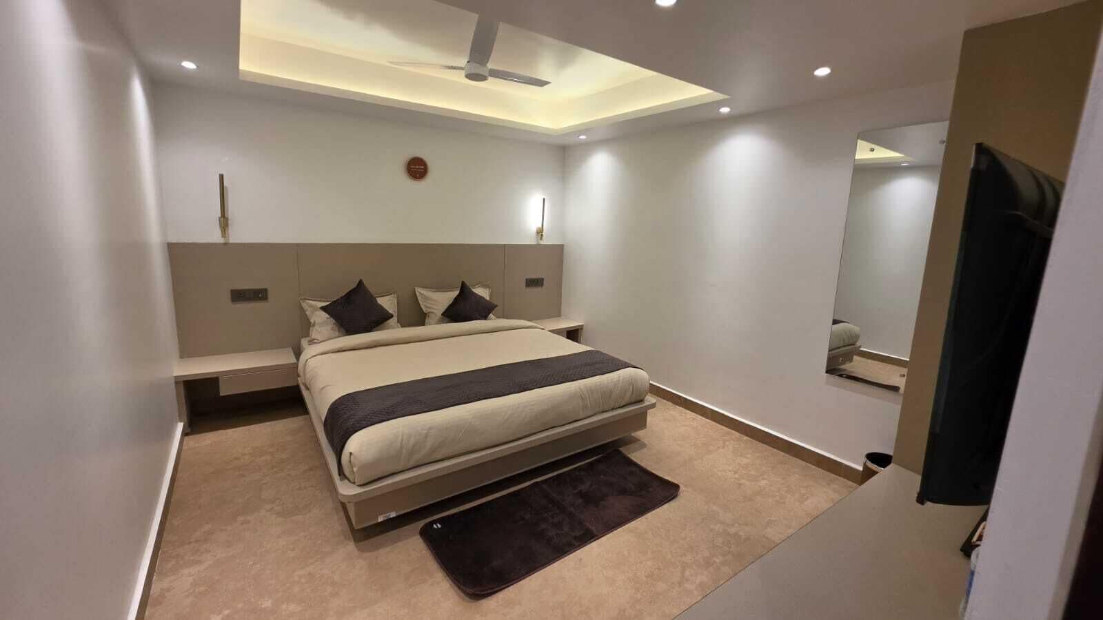 A modern bedroom with a bed, bedside tables, a ceiling fan, and a large mirror.