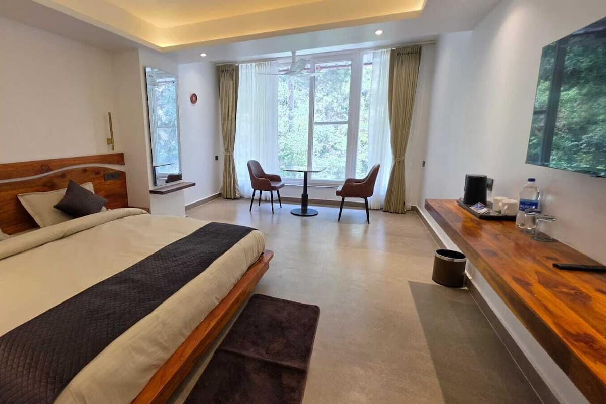 A modern hotel room with a large bed, a desk with a chair, a small table, and a large window.