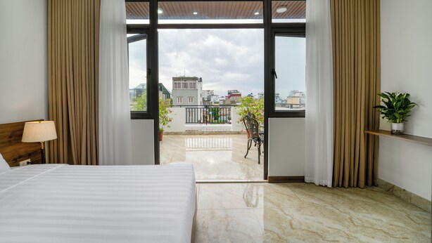 Ein Hotelzimmer mit einem Bett, einem Nachttisch, einer Lampe, einem Balkon mit Stadtblick und einer Topfpflanze.