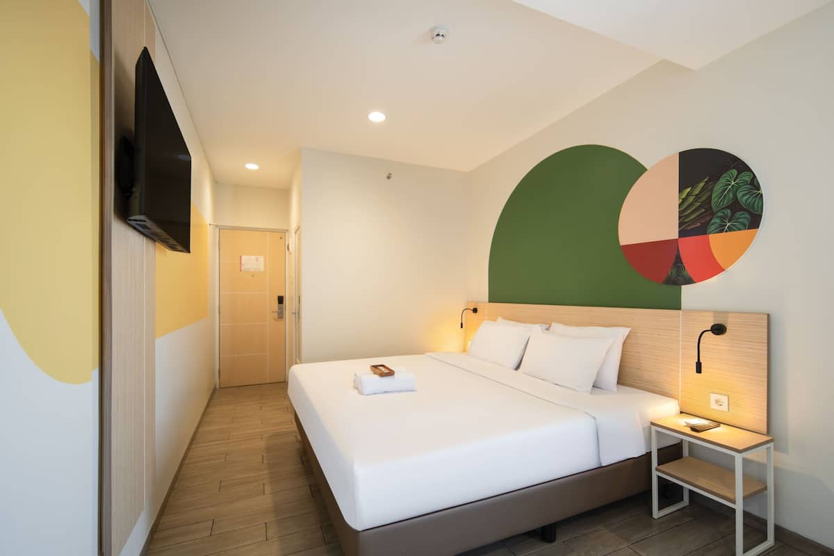 A hotel room with a bed, bedside table, wall-mounted TV, and a door leading to another room.