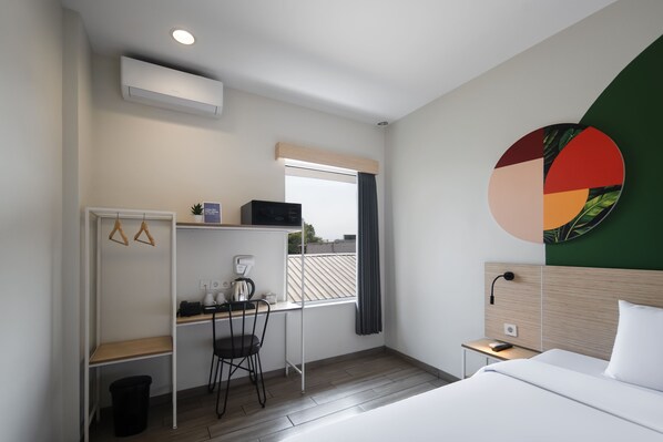 A hotel room with a bed, desk, chair, and a wall-mounted TV.