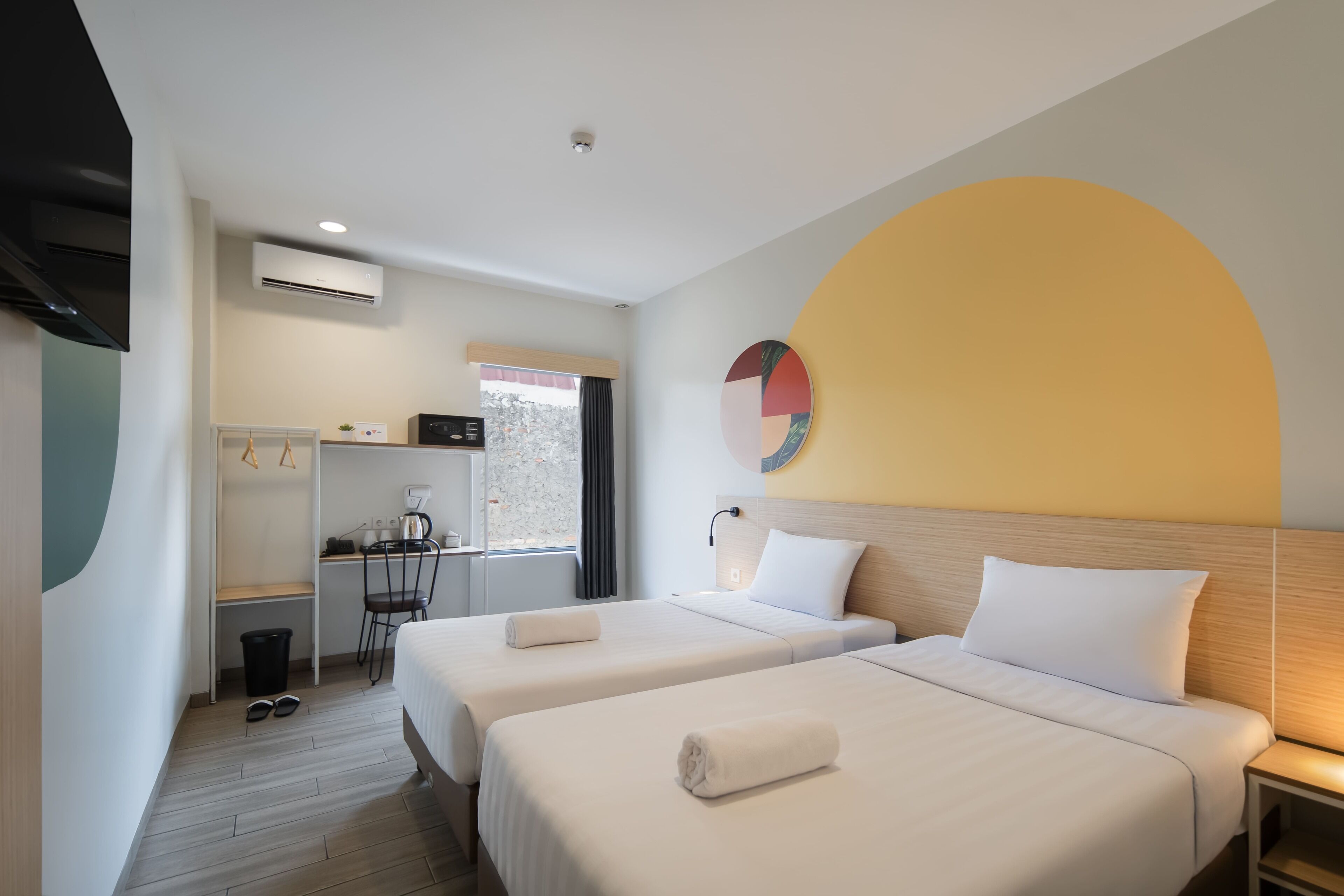 Ein Hotelzimmer mit zwei Betten, einem Schreibtisch, einem Stuhl und einem Fenster.