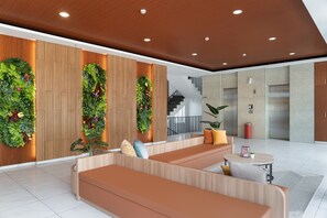 A modern lobby with wooden panel walls, green vertical gardens, and a seating area with orange sofas and a small round table.