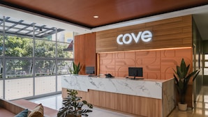 Una recepción con un letrero que dice 'Cove', mostrador de mármol, paneles de madera y plantas en macetas.