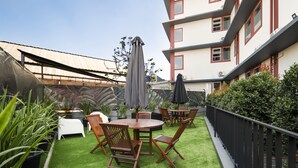 Una terraza en la azotea con mobiliario exterior, una chimenea y vistas a un edificio de varios pisos.