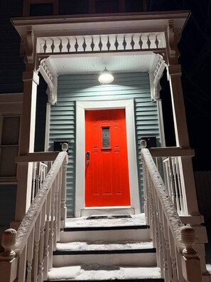 Ein Gebäude mit roter Tür, weißen Geländern und einer Veranda mit einer Lampe.