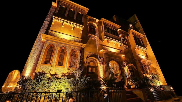 Um edifício grande e ornamentado, com várias arcadas e uma entrada imponente, iluminado durante a noite.