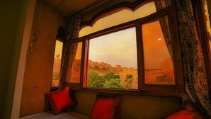 A room with a bed, a window with a view of a cityscape, and patterned curtains. - Hotel Golden Routes (Jaisalmer)