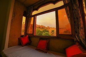 A room with a bed, a window with a view of a cityscape, and patterned curtains. - Hotel Golden Routes (Jaisalmer)