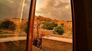 A view through a window of a building with a courtyard, stone walls, and a distant hill with buildings. - Hotel Golden Routes (Jaisalmer)