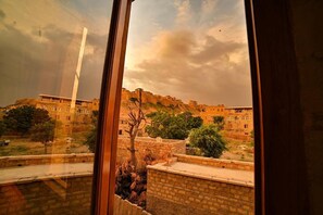 A view through a window of a building with a courtyard, stone walls, and a distant hill with buildings. - Hotel Golden Routes (Jaisalmer)
